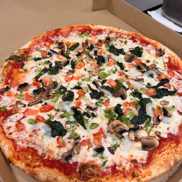 A whole vegetarian pizza with mushrooms, spinach, onions, and tomatoes in a cardboard box.