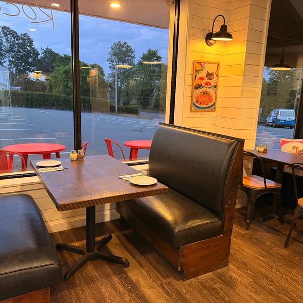 Cozy restaurant interior with booth seating and tables, viewed from inside looking out a large window.