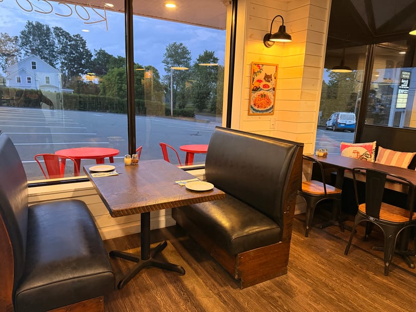Cozy restaurant interior with booth seating and tables, viewed from inside looking out a large window.