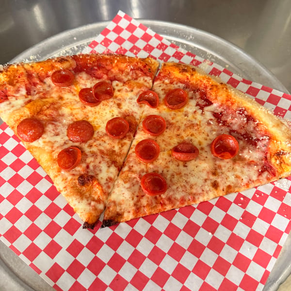 Two slices of pepperoni pizza on red and white checkered paper, on a metal pizza pan.