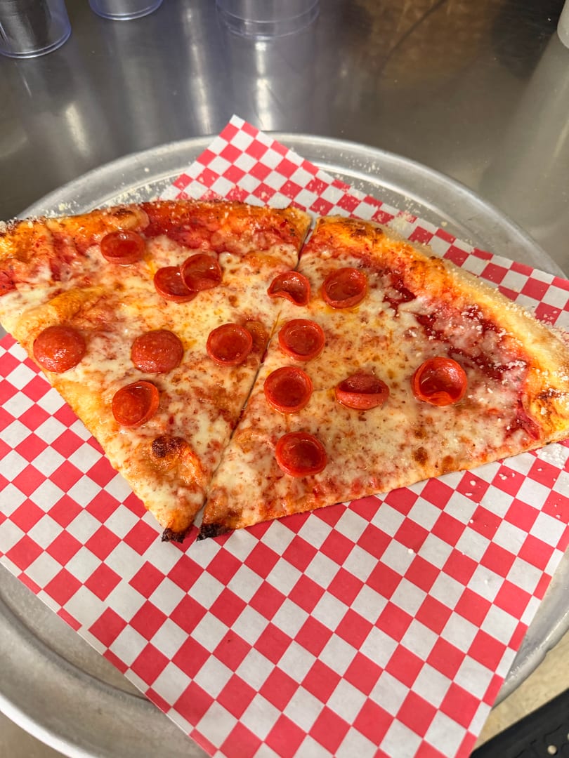 Two slices of pepperoni pizza on red and white checkered paper, on a metal pizza pan.