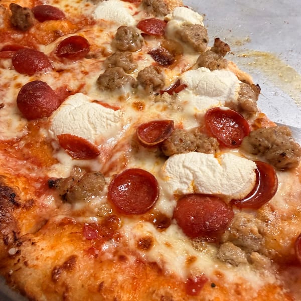 Close-up of a pizza slice with pepperoni, sausage, and dollops of ricotta cheese.