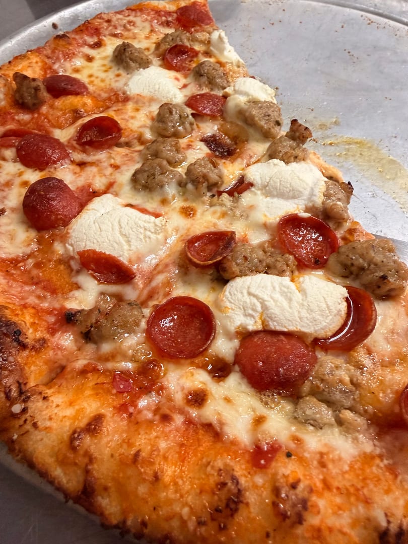 Close-up of a pizza slice with pepperoni, sausage, and dollops of ricotta cheese.