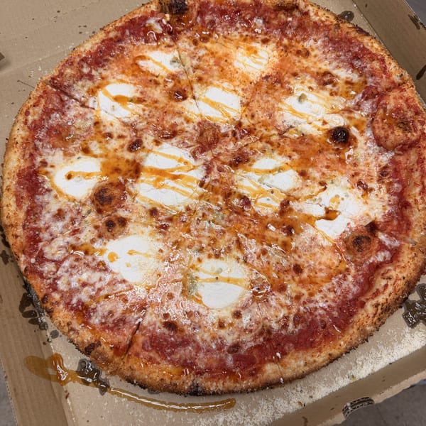 A whole pizza with tomato sauce, mozzarella, and a drizzle of hot honey in a cardboard box.