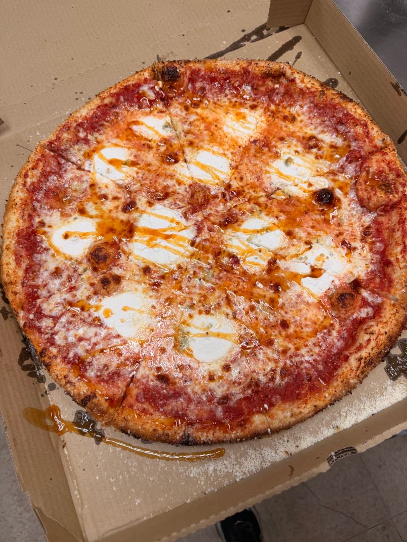 A whole pizza with tomato sauce, mozzarella, and a drizzle of hot honey in a cardboard box.