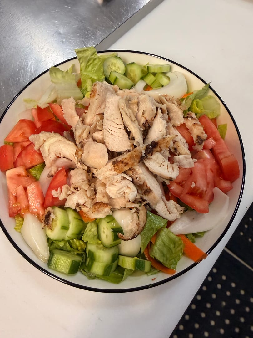 A large salad with grilled chicken, lettuce, tomatoes, cucumbers, and onions in a white bowl.