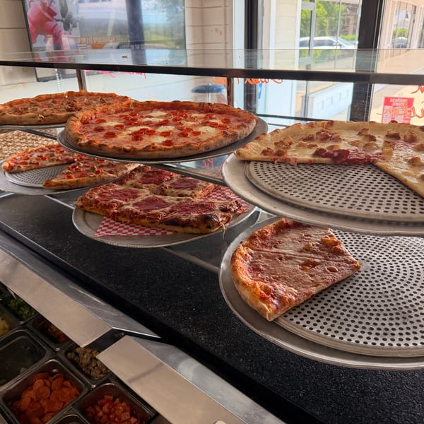 Various pizzas and slices, including pepperoni and plain cheese, displayed in a glass case.