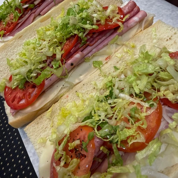 Several flatbread sandwiches filled with ham, salami, lettuce, tomatoes, onions, and cheese on a paper-lined tray.