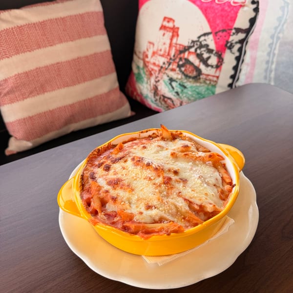 Baked penne pasta with melted cheese and tomato sauce in a yellow dish on a dark table.