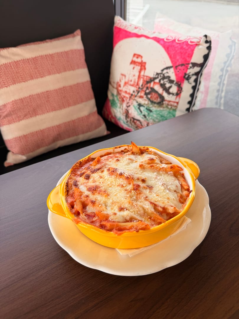 Baked penne pasta with melted cheese and tomato sauce in a yellow dish on a dark table.